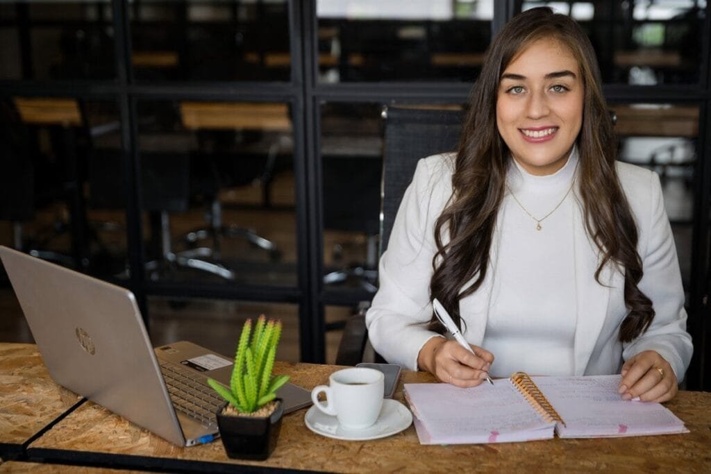 Mujer sonriente trabajando en su oficina moderna, con un cuaderno en la mano.