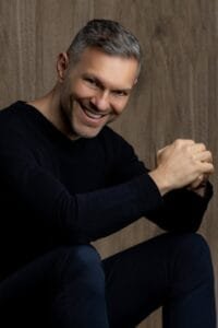 Hombre sonriendo en fondo de madera, mostrando una actitud amigable y profesional