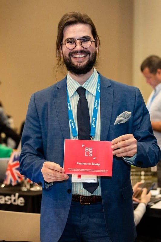 Hombre sonriente en un evento empresarial sostiene una tarjeta roja con el lema "Pasión por aprender".