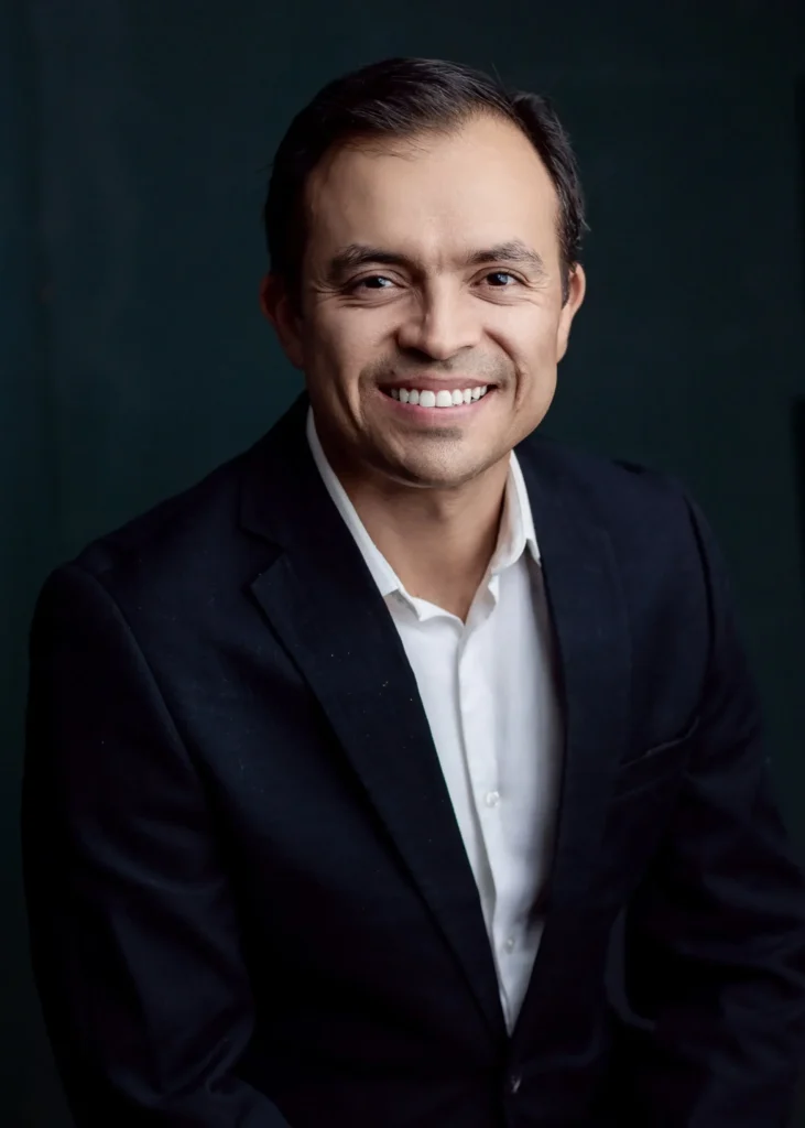 Retrato profesional de un hombre sonriente con traje oscuro.